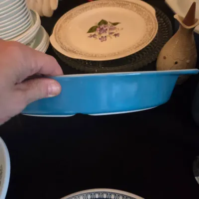 Sale Photo Thumbnail #114: Vintage Pyrex turquoise blue oval divided casserole dish held up above a selection of decorative plates and dishware.