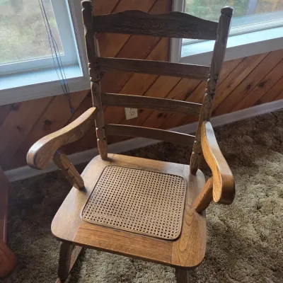 Sale Photo Thumbnail #77: Vintage ladder-back wooden rocking chair featuring carved floral detail on the crest rail and an inlaid woven cane seat panel.