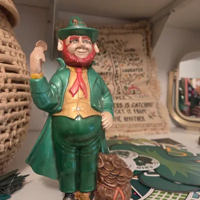 Sale Photo Thumbnail #137: Vintage painted ceramic leprechaun figurine standing beside a pot of gold while holding a gold coin.