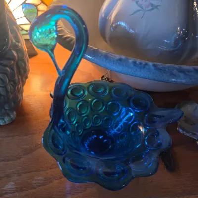 Sale Photo Thumbnail #101: Vintage blue glass swan-shaped bowl featuring a coin dot pattern, displayed on a wooden surface alongside other collectible ceramics.
