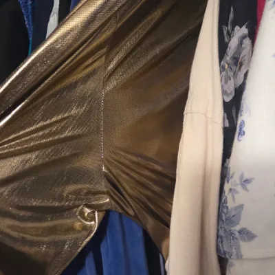 Sale Photo Thumbnail #66: Metallic gold garment featuring a batwing or dolman sleeve construction, hanging in a closet among other clothing items.