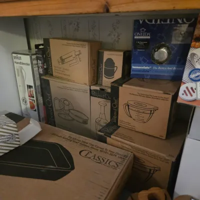Sale Photo Thumbnail #94: Collection of boxed kitchen gadgets and cookware including Pampered Chef items, a Braun hand blender, and an Oneida saucepan cover.
