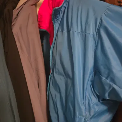 Sale Photo Thumbnail #57: Vintage blue nylon windbreaker jacket with a bright pink collar lining, hanging alongside other coats in a closet.