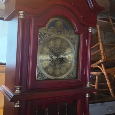 Sale Photo Thumbnail #31: Traditional mahogany-finished grandfather clock featuring a bonnet top, ornate brass dial with Roman numerals, and a moon phase disk.