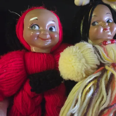 Sale Photo Thumbnail #41: Pair of vintage handmade yarn dolls featuring painted plastic faces, including one in red and one in yellow and multi-colored threads.
