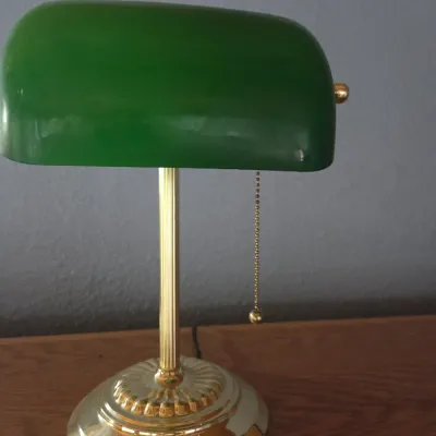 Sale Photo Thumbnail #82: Classic banker's desk lamp featuring a green glass shade, polished brass-finish base, and a bead-chain pull switch.