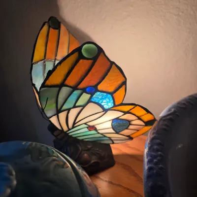 Sale Photo Thumbnail #103: Tiffany-style stained glass butterfly accent lamp featuring vibrant orange, blue, and cream panels set on a dark metal base.