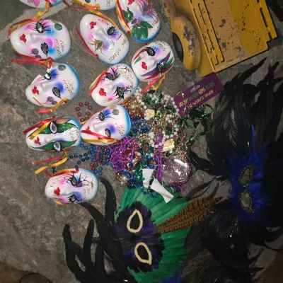 Sale Photo Thumbnail #70: Collection of Mardi Gras souvenirs, including hand-painted porcelain face masks, feathered eye masks, and colorful beaded necklaces.