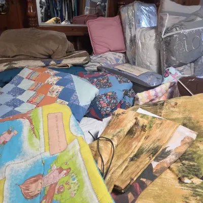 Sale Photo Thumbnail #143: Large assortment of vintage and modern bedding, including handmade quilts, Holly Hobbie fabric, comforters, and packaged pillows resting on a wooden bed frame.