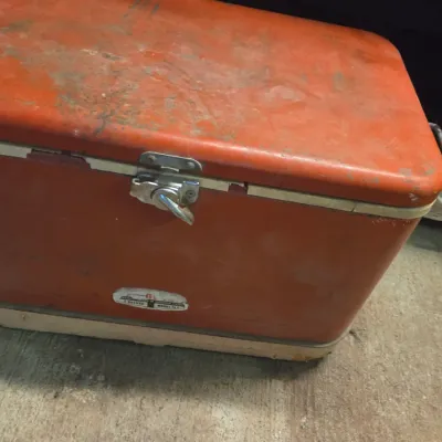 Sale Photo Thumbnail #20: Vintage orange and white metal cooler with a front latch mechanism, showing age-appropriate surface wear and patina.