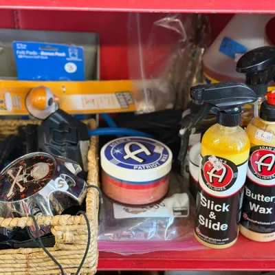 Sale Photo Thumbnail #13: Collection of car detailing supplies including Adam's Polishes waxes and sprays, set alongside a woven storage basket with automotive accessories.
