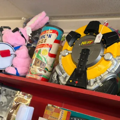 Sale Photo Thumbnail #11: Collection of vintage toys and novelties displayed on a red shelf, including a Nerf target game, an Energizer Bunny plush, and a vintage American Logs building set canister.