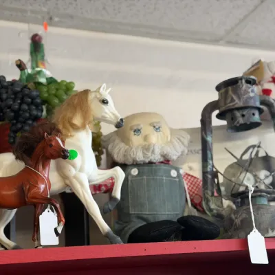 Sale Photo Thumbnail #10: Shelf display of assorted collectibles including model horses, a handcrafted stuffed figure in denim overalls, and a camouflage lantern.
