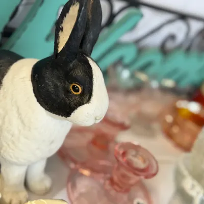 Sale Photo Thumbnail #19: Hand-painted black and white resin rabbit figurine, shown alongside various vintage glassware items including pink depression glass candlesticks.