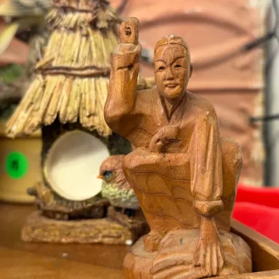 Sale Photo Thumbnail #27: Hand-carved wooden figurine of a crouching Asian elder alongside a decorative rustic hut birdhouse sculpture.