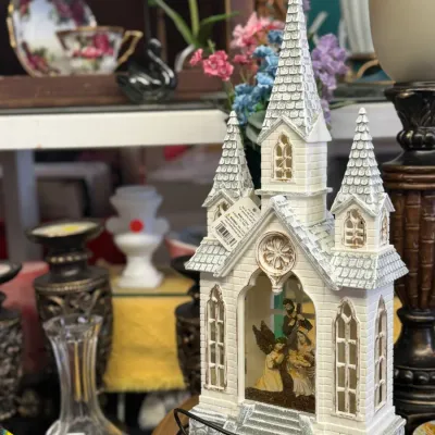 Sale Photo Thumbnail #22: White church-shaped glitter globe depicting a Nativity scene inside, featuring three spires and an attached power cord.