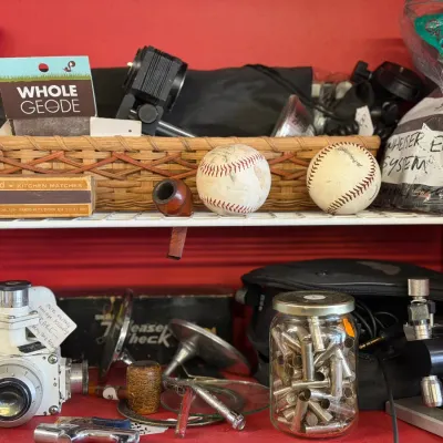 Sale Photo Thumbnail #12: Collection of vintage oddities and collectibles, including baseballs, a tobacco pipe, a box of Diamond matches, and a vintage military periscope sight unit on shelves.