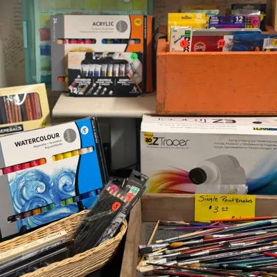 Sale Photo Thumbnail #35: Assorted art supplies including watercolor paint sets, an Artograph EZ Tracer projector, pencils, and a tray of loose paintbrushes.