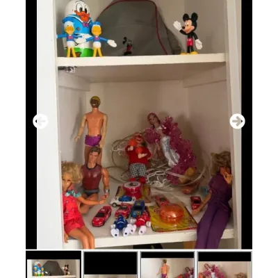 Sale Photo Thumbnail #97: Collection of vintage toys including Disney figurines, Donald Duck nesting doll, fashion dolls, and toy die-cast cars arranged on white shelves.