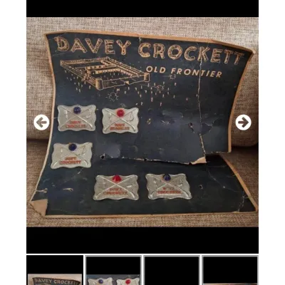 Vintage 1950s Davy Crockett Old Frontier belt buckles mounted on original illustrated cardboard display card showing significant age wear.