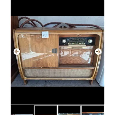 Sale Photo Thumbnail #76: Vintage mid-century wooden radio console cabinet featuring a multi-band tuner, sliding door compartment, and woven speaker grille with visible finish wear.