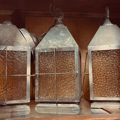 Set of three vintage hanging lantern light fixtures featuring aged metal frames and amber bubble glass panels.