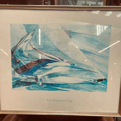 Sale Photo Thumbnail #20: Framed America's Cup art print featuring an abstract blue and white sailboat composition, mounted in a silver-toned frame with glass.