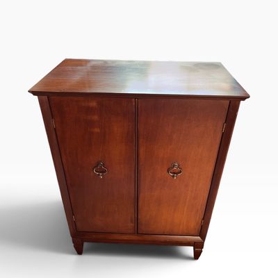 Vintage dark wood two-door storage cabinet featuring brass drop handle pulls and short tapered legs.