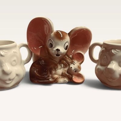 Vintage ceramic mouse figurine flanked by two matching novelty character mugs with double handles.