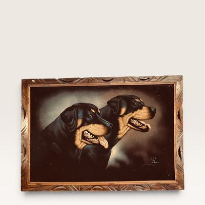 Vintage black velvet oil painting depicting two Rottweilers, signed in the lower right corner and set in a carved wooden frame.