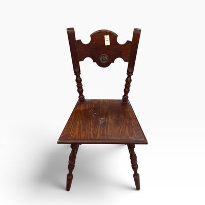 Vintage dark oak side chair featuring turned spindle legs, a shaped splat back with carved rosette details, and visible surface wear.