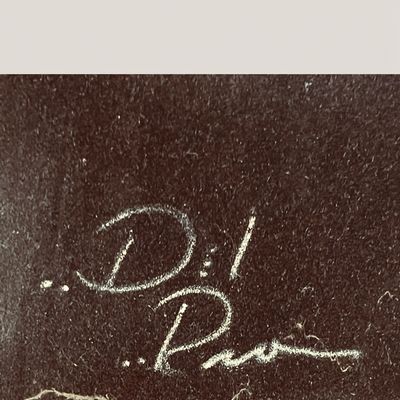Close-up detail of an artist's signature reading Del Rio, rendered in white on a dark textured background.