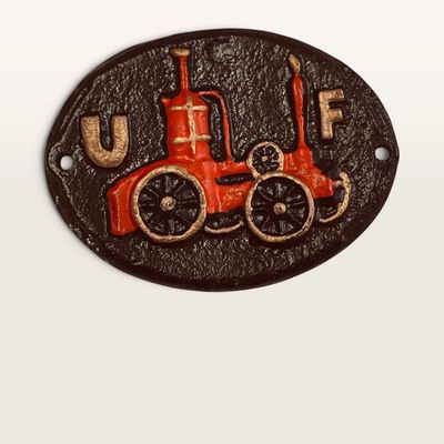 Vintage painted cast iron oval wall plaque featuring a raised red and gold steam tractor motif with the letters 'U' and...