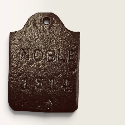 Vintage dark brown cast iron tag or weight featuring embossed lettering that reads NOBLE and the number 1514, with a top hanging hole.