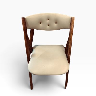 Mid-century wooden folding chair featuring cream-colored vinyl upholstery with button-tufted backrest detail.