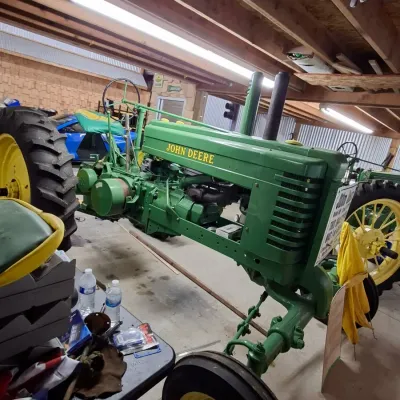 Sale Photo Thumbnail #3: Vintage restored green and yellow John Deere tractor, parked indoors alongside workshop equipment.