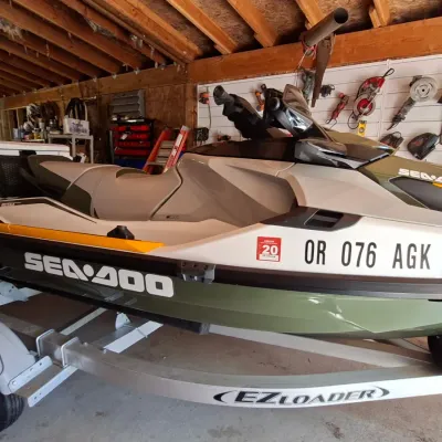 Sale Photo Thumbnail #7: Modern Sea-Doo personal watercraft in white, olive green, and yellow trim, sitting on an EZ Loader single-axle boat trailer inside a garage.
