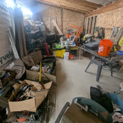 Sale Photo Thumbnail #11: Workshop space filled with various power tools, hardware, storage bins, an orange engine hoist, and a table saw.