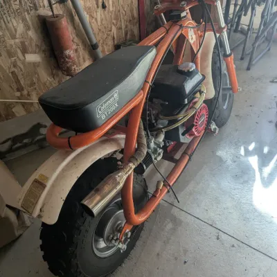 Sale Photo Thumbnail #13: Orange Coleman Powersports BT20X mini bike featuring a padded black vinyl seat, rear exhaust modification, and knobby off-road tires.