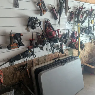 Sale Photo Thumbnail #16: Workshop wall filled with assorted power tools, including nail guns, circular saws, and routers, and more 