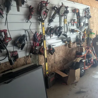 Sale Photo Thumbnail #15: Slatwall tool organization system filled with various power tools, including circular saws, angle grinders, and nail guns, alongside a small orange minibike.
