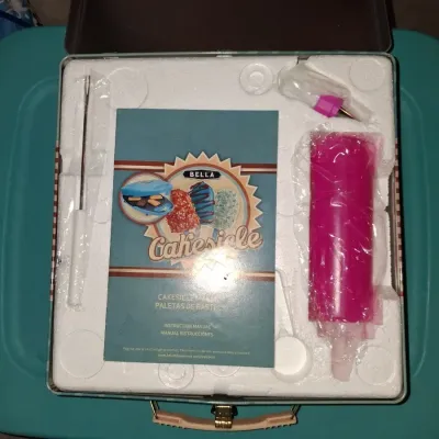 Sale Photo Thumbnail #681: BELLA CAKESICLE MAKER IN ORIGINAL TIN LUNCHBOX STYLE STORAGE BOX. INCLUDES MAKER, INSTRUCTION MANUAL, DECORATING SYRINGE TOOL, STICKS AND MORE. APPEARS LIGHTLY USED OR UNUSED IN ORIGINAL PACKAGING.