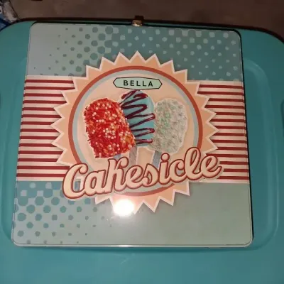 Sale Photo Thumbnail #679: BELLA CAKESICLE MAKER IN ORIGINAL TIN LUNCHBOX STYLE STORAGE BOX. INCLUDES MAKER, INSTRUCTION MANUAL, DECORATING SYRINGE TOOL, STICKS AND MORE. APPEARS LIGHTLY USED OR UNUSED IN ORIGINAL PACKAGING.
