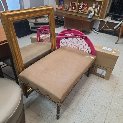 Sale Photo Thumbnail #14: Tan fabric-upholstered bench with decorative nailhead trim and turned wooden legs, positioned in front of a large gold-framed mirror.