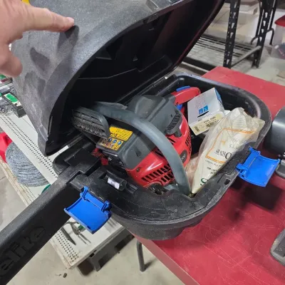 Sale Photo Thumbnail #108: Red and black Homelite gas-powered chainsaw packed inside its original hard plastic carrying case with blue latches.