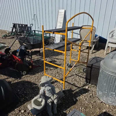 Sale Photo Thumbnail #143: Yellow rolling baker's scaffold with black wooden platforms, displayed alongside various outdoor equipment, garden decor, and lawn care items.