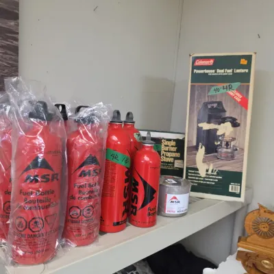 Sale Photo Thumbnail #51: Selection of red MSR liquid fuel bottles, camping kettles, and boxed Coleman camping equipment including a Dual Fuel lantern and single-burner stove.