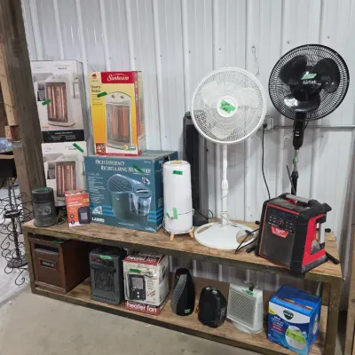 Sale Photo Thumbnail #111: Collection of small household appliances including space heaters, standing fans, humidifiers, and a jobsite radio arranged on a wooden shelving unit.