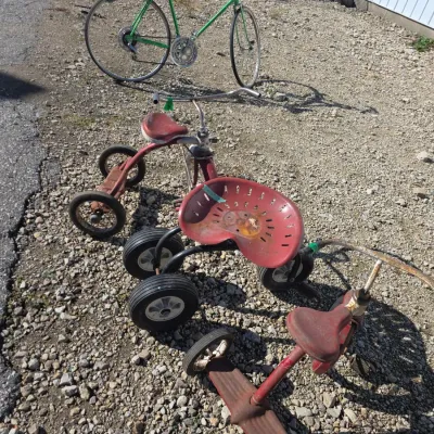 Sale Photo Thumbnail #146: Collection of vintage wheeled items, including a green 10-speed road bicycle, red metal tricycles, and a custom tractor-seat kart, all showing play-worn condition.