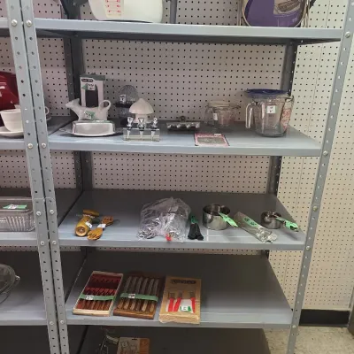 Sale Photo Thumbnail #37: Metal shelving unit holding various kitchenware, including measuring cups, boxed cutlery sets, a butter dish, and vintage gadgets.